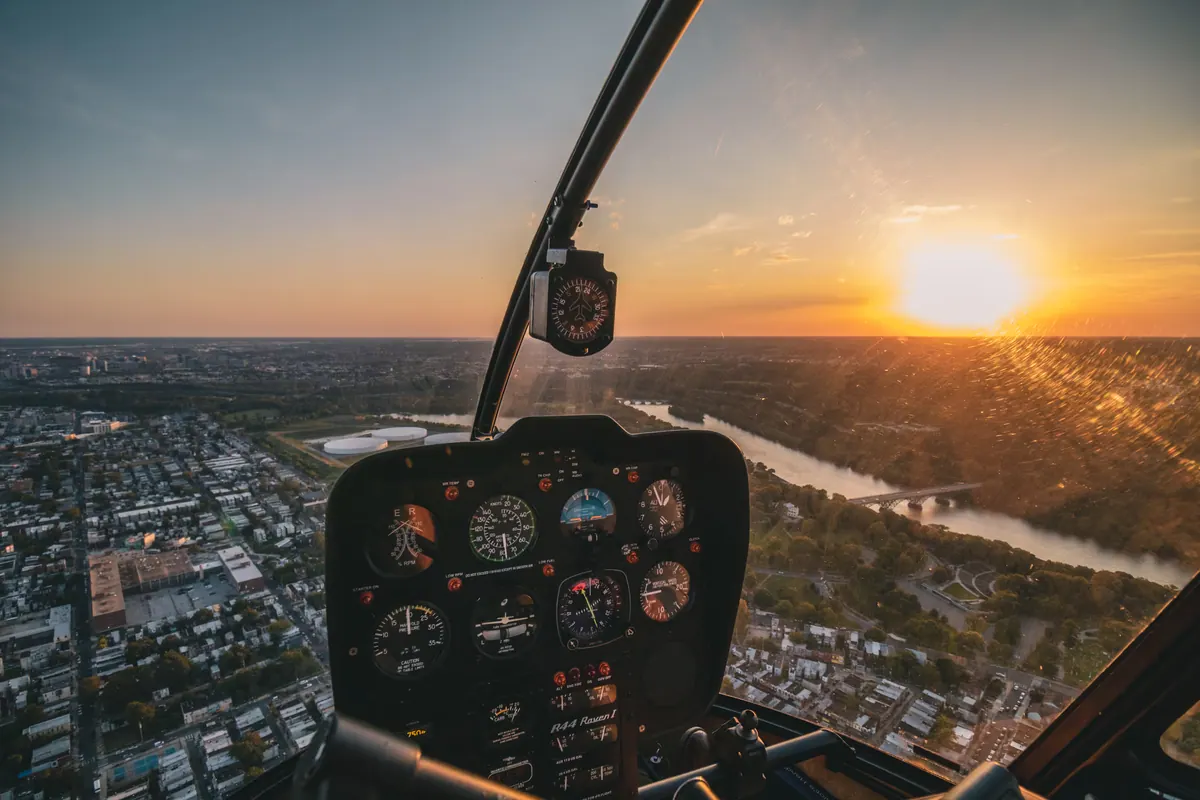 The sun setting over a city and a river, seen through a helicopter windscreen past the instrument panel